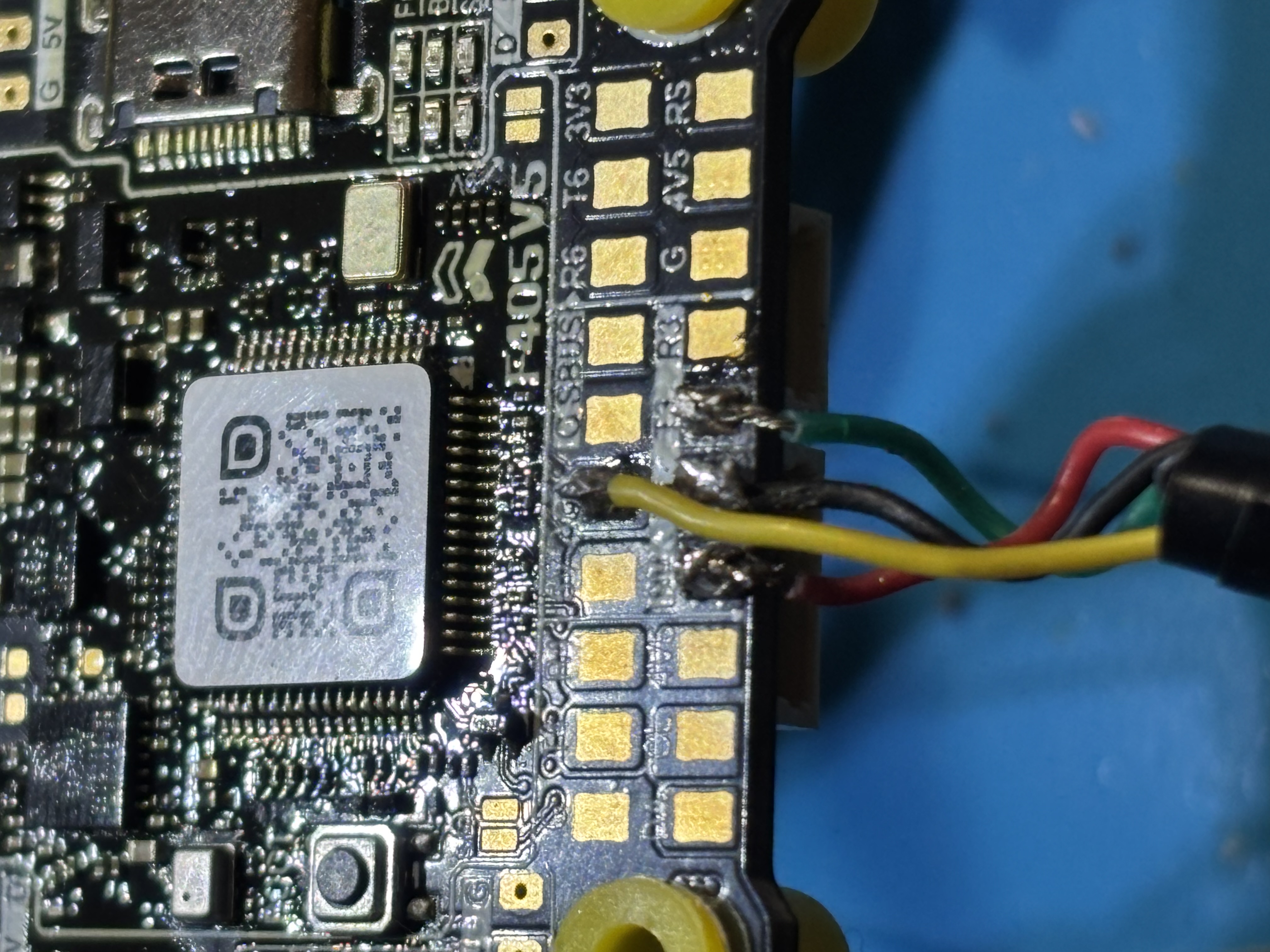 Macro close-up of the SpeedyBee F405 flight controller pads with signal wires soldered to the UART pads