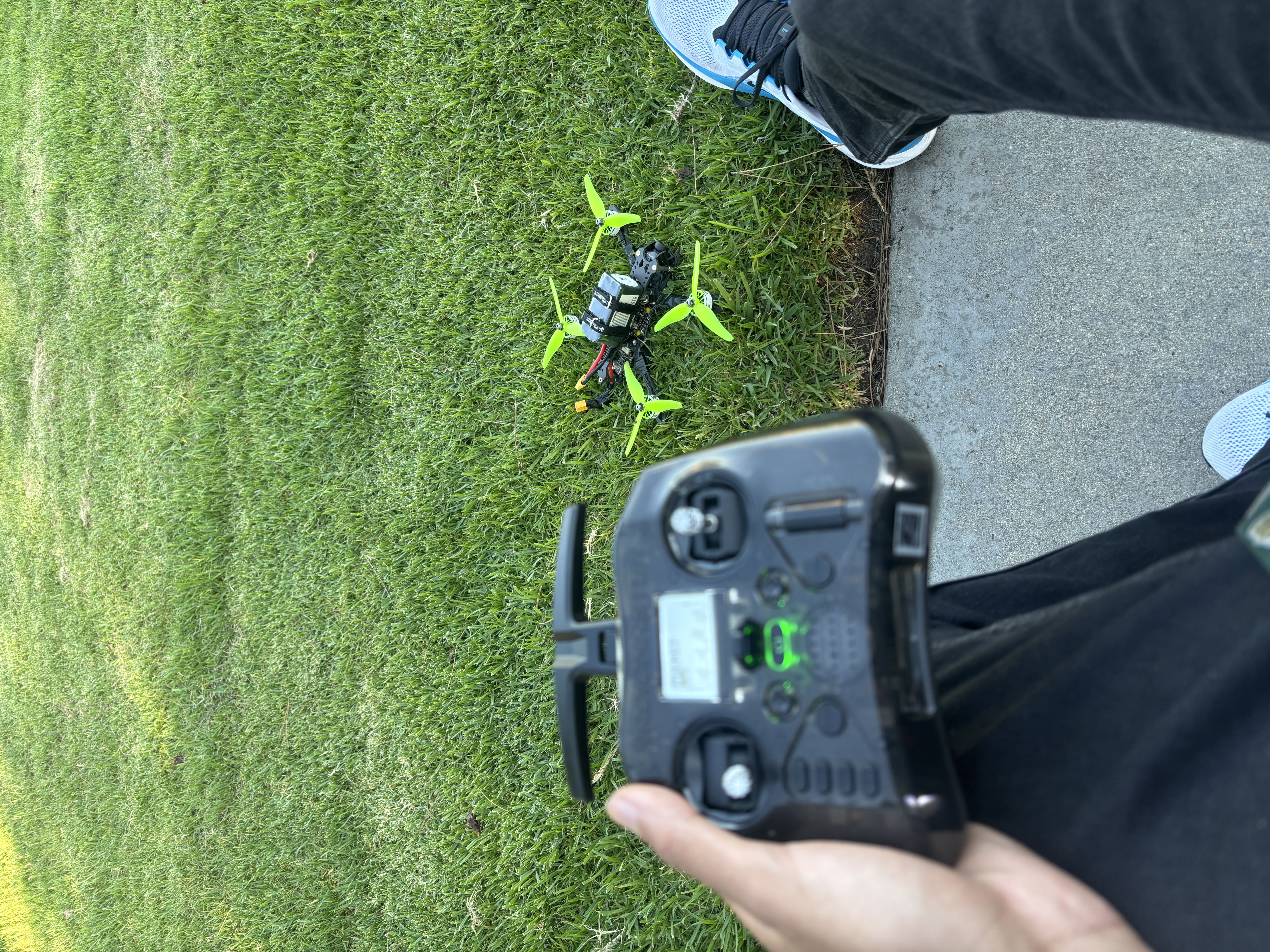 The finished FPV drone in the grass next to the RadioMaster Pocket ELRS transmitter during a field test